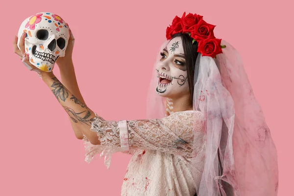 ピンクの背景に人間の頭蓋骨を描いたハロウィンパーティーのための死んだ花嫁として服を着た若い女性 — ストック写真