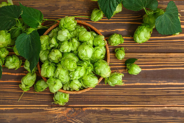 Bowl with fresh green hops and leaves on wooden background