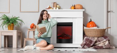 Evde şöminenin yanında kitap okuyan genç bir kadın.