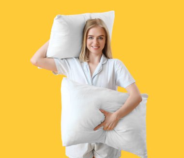 Pijamalı ve sarı arka planda yastıkları olan mutlu genç bir kadın.