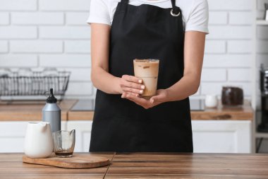 Mutfaktaki ahşap masada bir bardak lezzetli kahve tutan bayan barista.