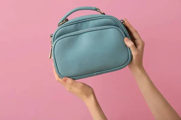 Female hands with stylish blue handbag on pink background