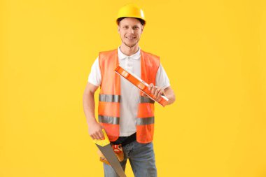 Male worker with builder's level on yellow background