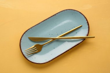 Altın çatal ve turuncu arka planda mavi plaka.
