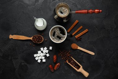 Bir fincan lezzetli kahve, fasulye, pudra, şeker, tarçın, kurutulmuş hurma ve siyah arka planda süt ile cezalandırılırlar.