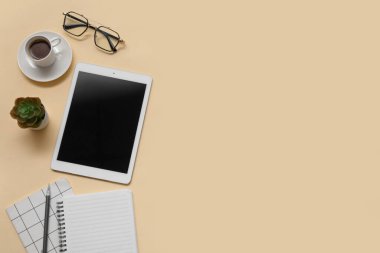 Tablet, bir fincan kahve ve bej arka planda kırtasiye malzemesi