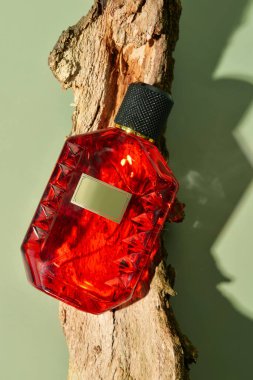 Kırmızı parfüm şişesi ve yeşil arka planda ağaç kabuğu.