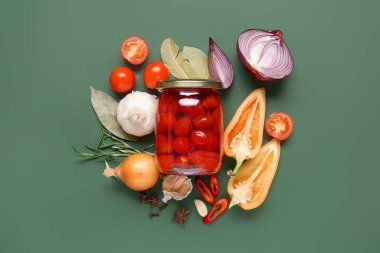 Bir kavanoz domates turşusu ve yeşil arka planda farklı sebzeler.
