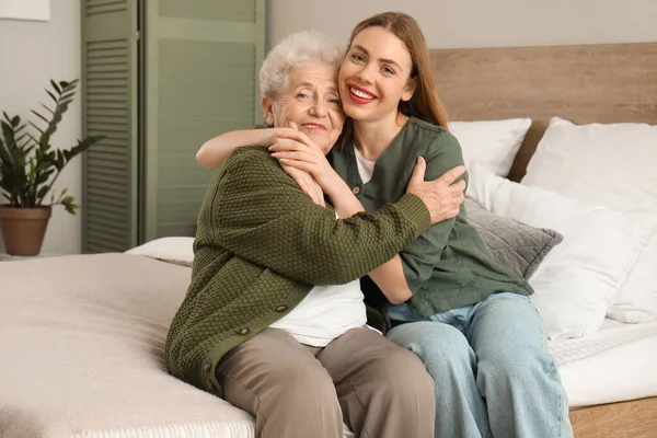 Young woman with her grandmother hugging in bedroom