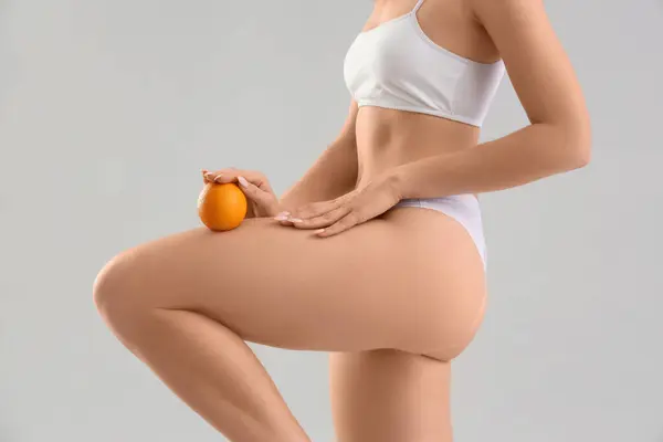 Young woman with cellulite problem and orange on light background, closeup