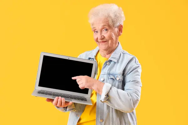 Mulher Sênior Apontando Para Laptop Branco Fundo Amarelo — Fotografia de Stock