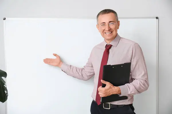 Male teacher with clipboard pointing at flipboard in classroom