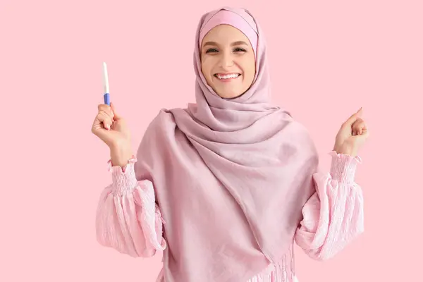 ピンクの背景で妊娠テストでヒジャブで幸せな美しい若い女性 — ストック写真