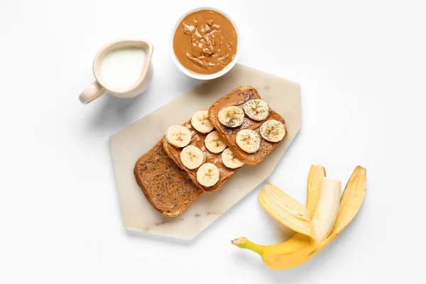 Board of toasts with peanut butter and banana on white background
