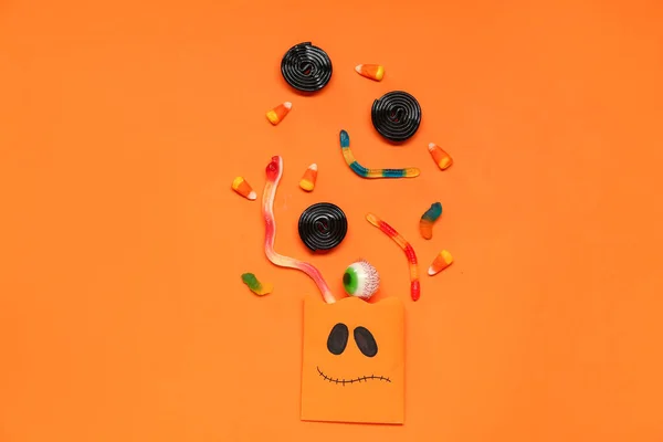 Halloween composition with paper bag and candies on orange background