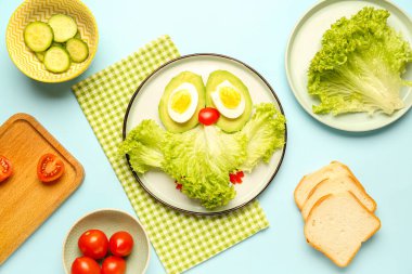 Baykuş şeklinde komik bir kahvaltı tabağı, mavi arka planda sebze ve ekmek.