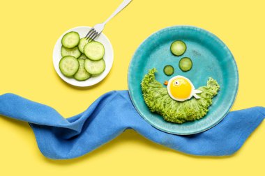 Sarı zemin üzerinde balık ve sebze şeklinde komik bir kahvaltı tabağı.