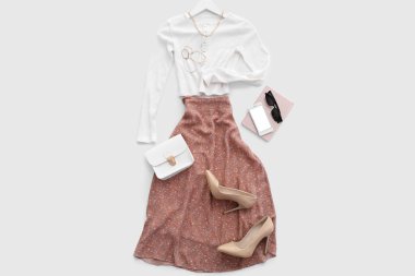 Aksesuarlı şık kıyafetler, topuklu ayakkabılar, cep telefonu ve beyaz arka planda not defteri.