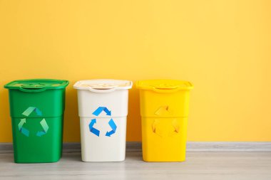 Sarı duvarın yanında geri dönüşüm sembolü olan farklı çöp bidonları