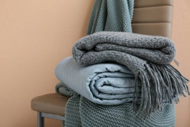 Bej duvarın yanındaki sandalyeye yeni katlanmış battaniyeler, yakın plan.