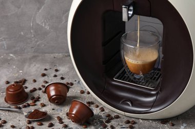 Damlayan espresso, fincan, kapsül kahve makinesi ve gri grunge masasında fasulye.