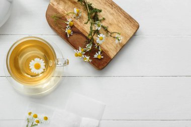 Beyaz ahşap arka planda bir fincan sıcak papatya çayı.