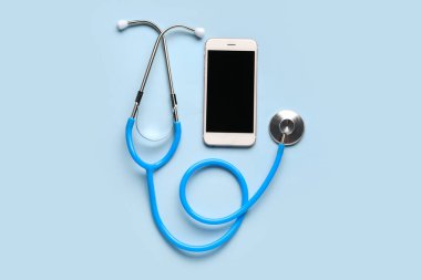 Açık mavi arkaplanda stetoskop ve cep telefonu