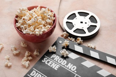 Lezzetli patlamış mısır, alkış tahtası ve arka planda film makarası olan bir kase.