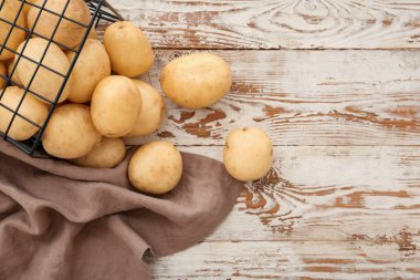 Beyaz ahşap arka planda çiğ patates dolu sepet.