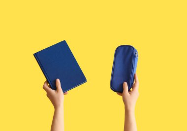 Sarı arka planda yazı defteri ve kalem çantası tutan kadın eller