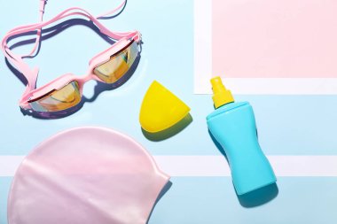 Renkli arka planda bir şişe güneş kremi, yüzme şapkası ve gözlük.