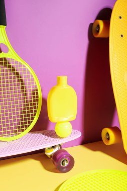 Güneş kremi, kaykay, tenis raketi ve renkli arka planda top içeren kompozisyon