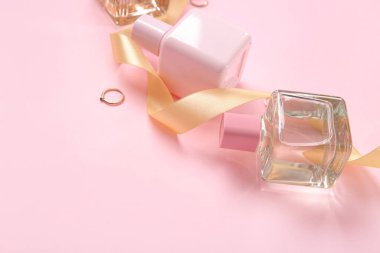 Pembe arka planda parfüm şişeleri, yüzükler ve altın kurdele.