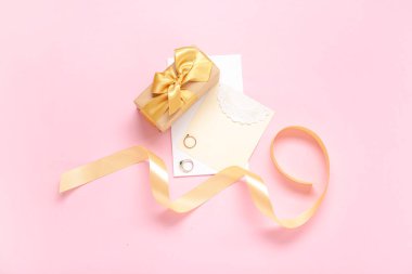 Hediye kutusu, yüzük ve pembe arka planda altın kurdele.
