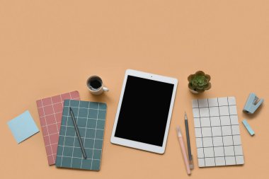 Tablet, bir fincan kahve ve kahverengi arka planda kırtasiye malzemesi.