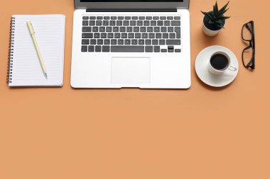 Laptop, bir fincan kahve ve kahverengi arka planda kırtasiye malzemesi.