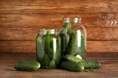 Ahşap arka planda konserve konserveler için taze salatalıklı kavanozlar.