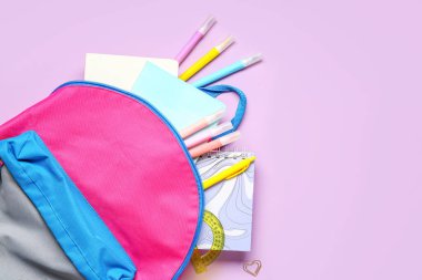 Leylak arka planında farklı kırtasiye malzemesi olan şık bir okul çantası