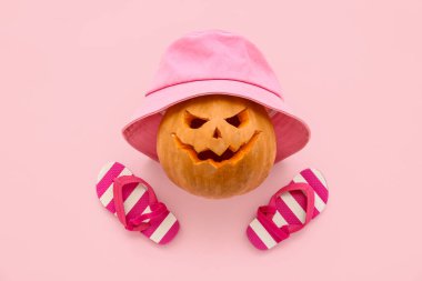 Cadılar Bayramı için oyulmuş kabak pembe arka planda şık şapkalar ve parmak arası terlikler.