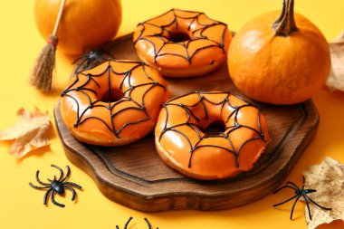 Sarı arka planda Cadılar Bayramı süslemeleri olan ahşap bir çörek tahtası.