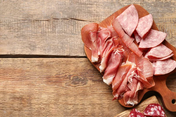 Board with assortment of tasty deli meats on wooden background