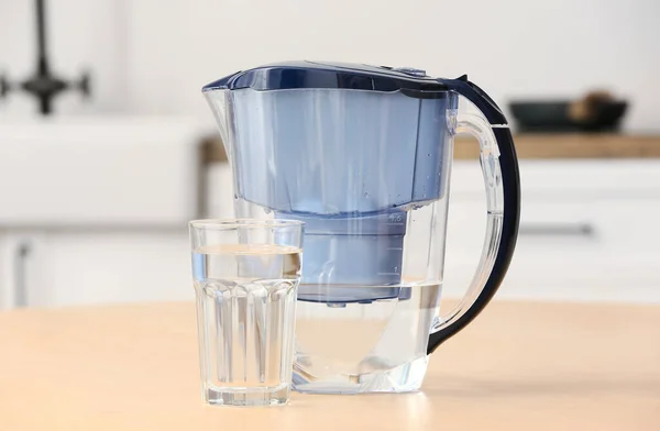 stock image Glass of pure water and filter jug on wooden table in kitchen