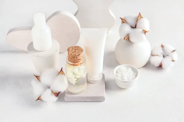 Composition with cosmetic products, plaster stands and cotton flowers on light table