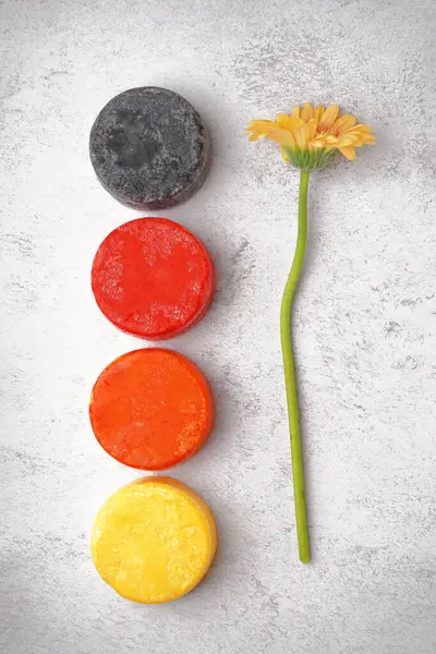 Different handmade solid shampoo and calendula flower on light background