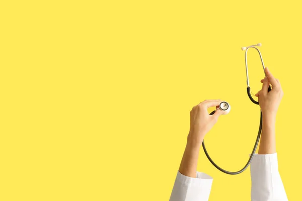 Female doctor\'s hands with stethoscope on yellow background