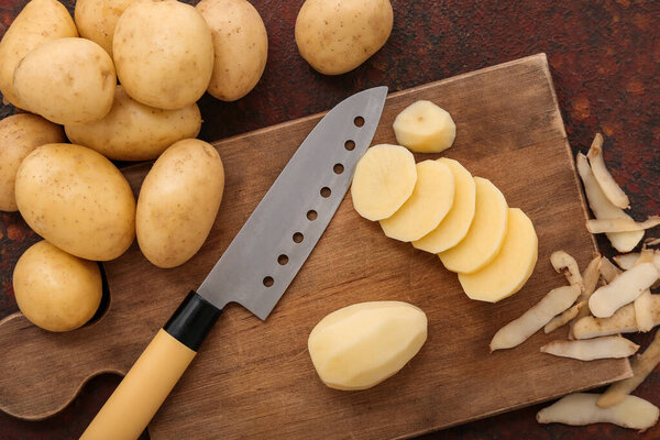 Сырой картофель и деревянная доска с ломтиками на темном фоне