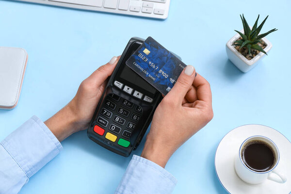 Female hands with credit card, payment terminal and cup of coffee on blue background