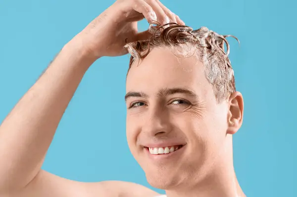 Young man washing hair against light blue background