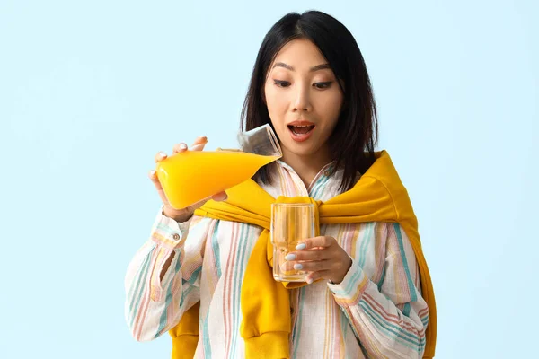 Beautiful Asian woman pouring juice into glass on blue background