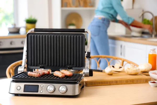 Tasty sausages in modern electric grill on table in kitchen